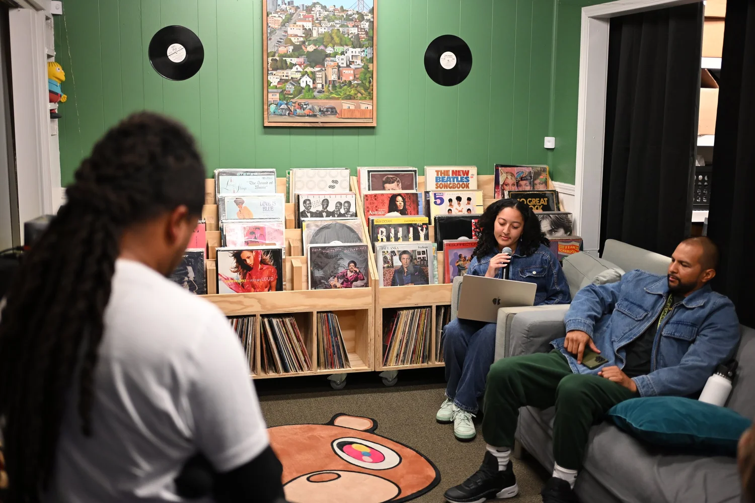 Musician and attendees gathered beside shelves of records and books.