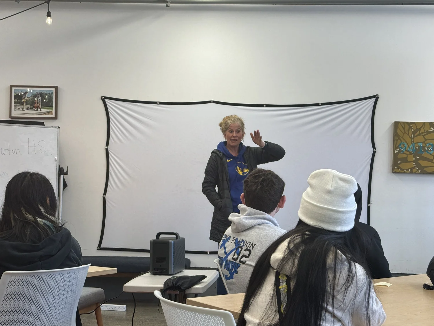 A presenter gestures beside a projection screen.