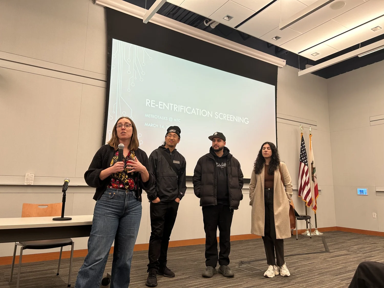 Documentary speakers stand in front of a projection screen.
