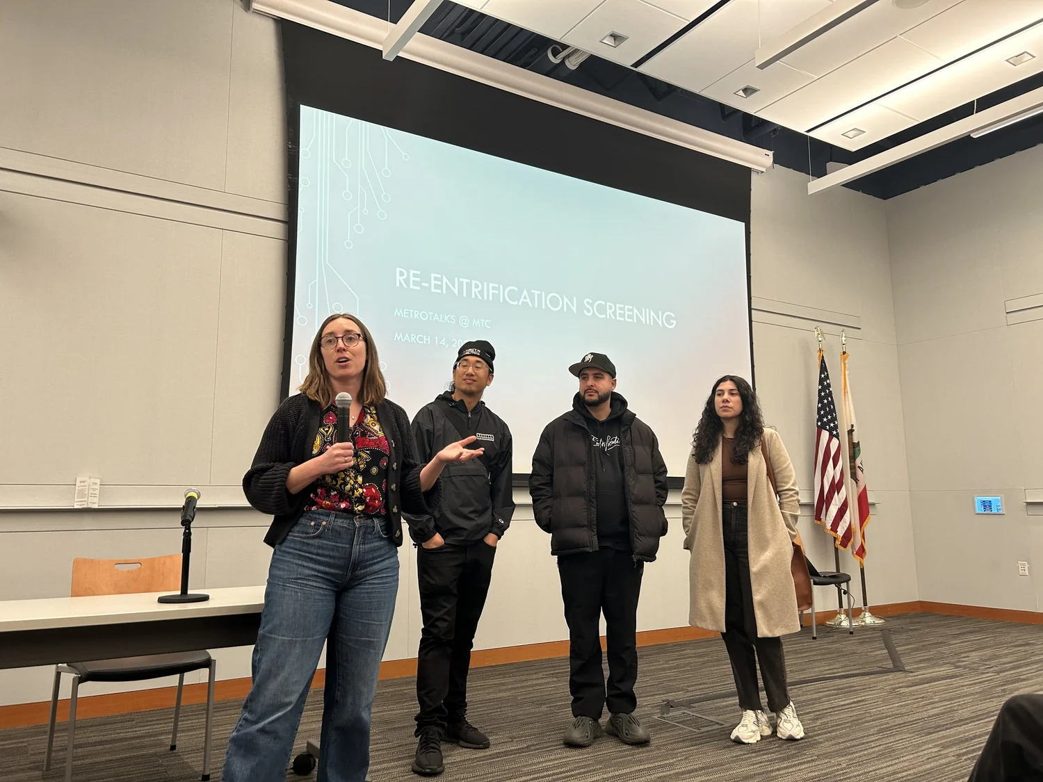 Documentary speakers stand in front of a projection screen.