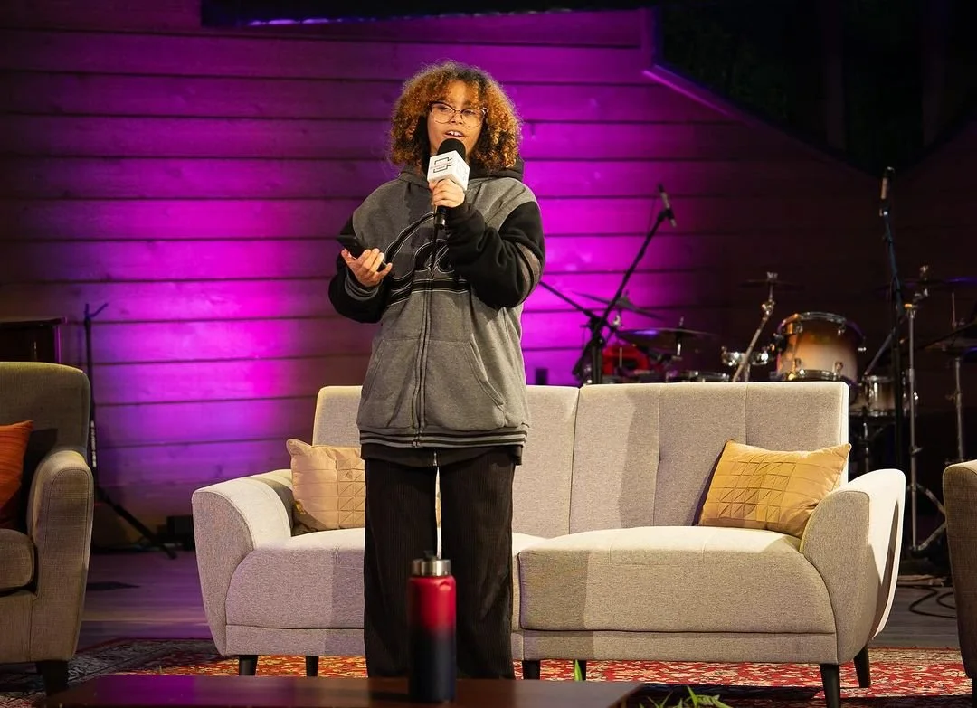 A speaker addresses the audience beside an armchair.