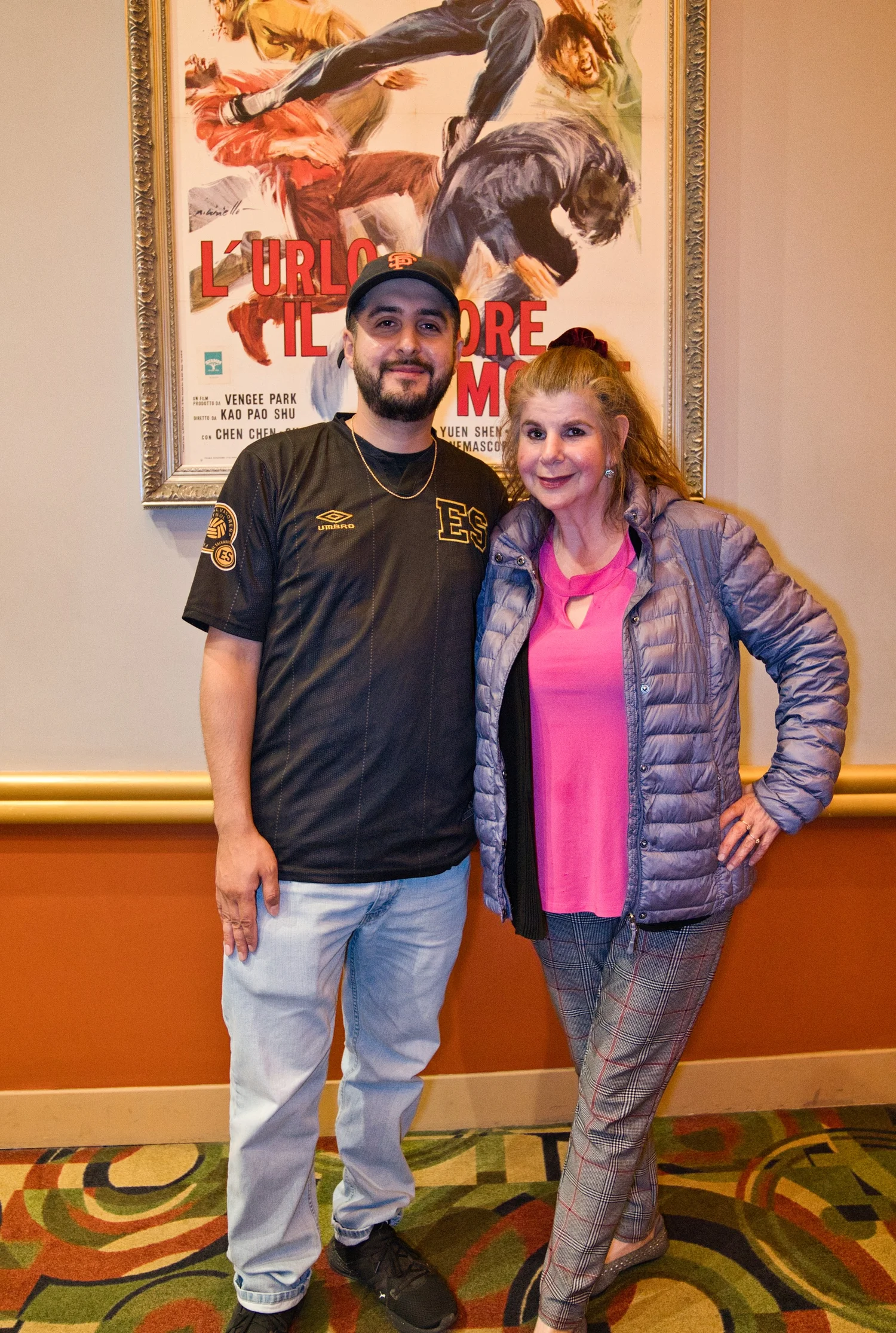 Two attendees posing beneath a theater poster.