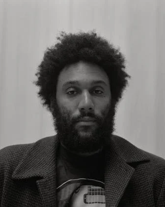 Black-and-white portrait of a bearded person in a dark jacket.