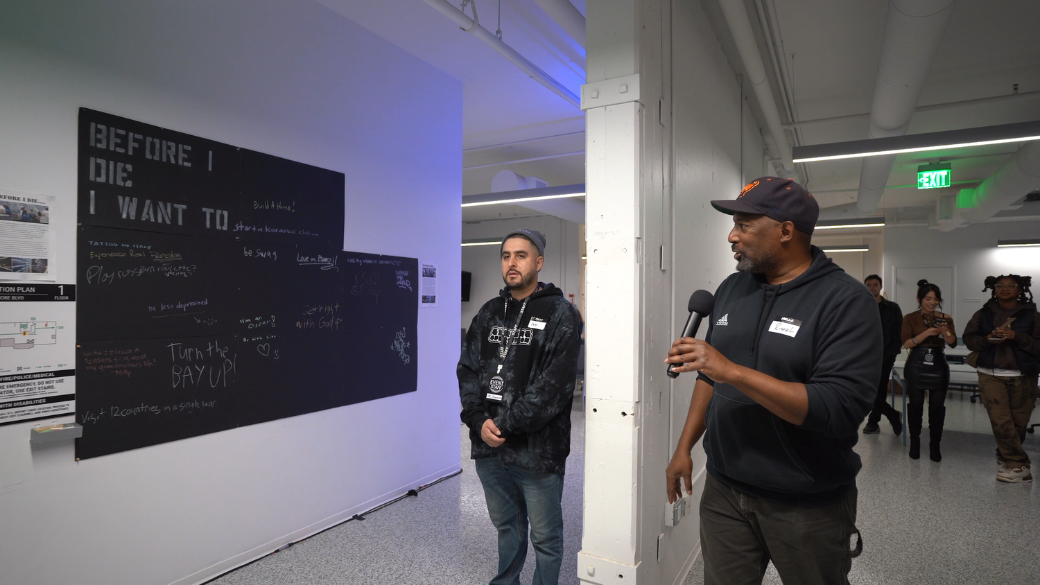 A presenter speaks next to the exhibition text panel.