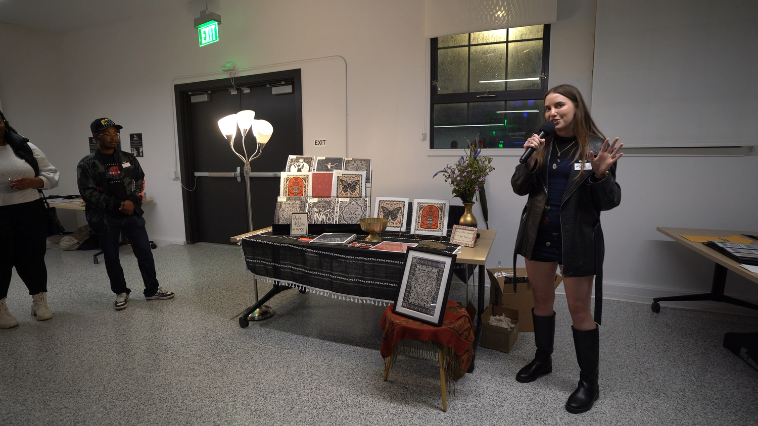 An artist speaks next to a display of framed prints.