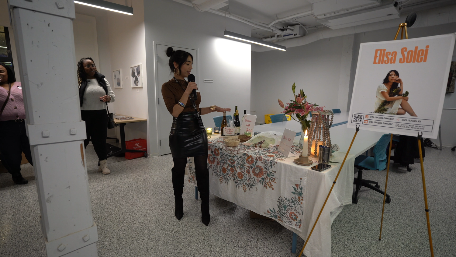 A performer stands beside an Elisa Solei poster and display table.