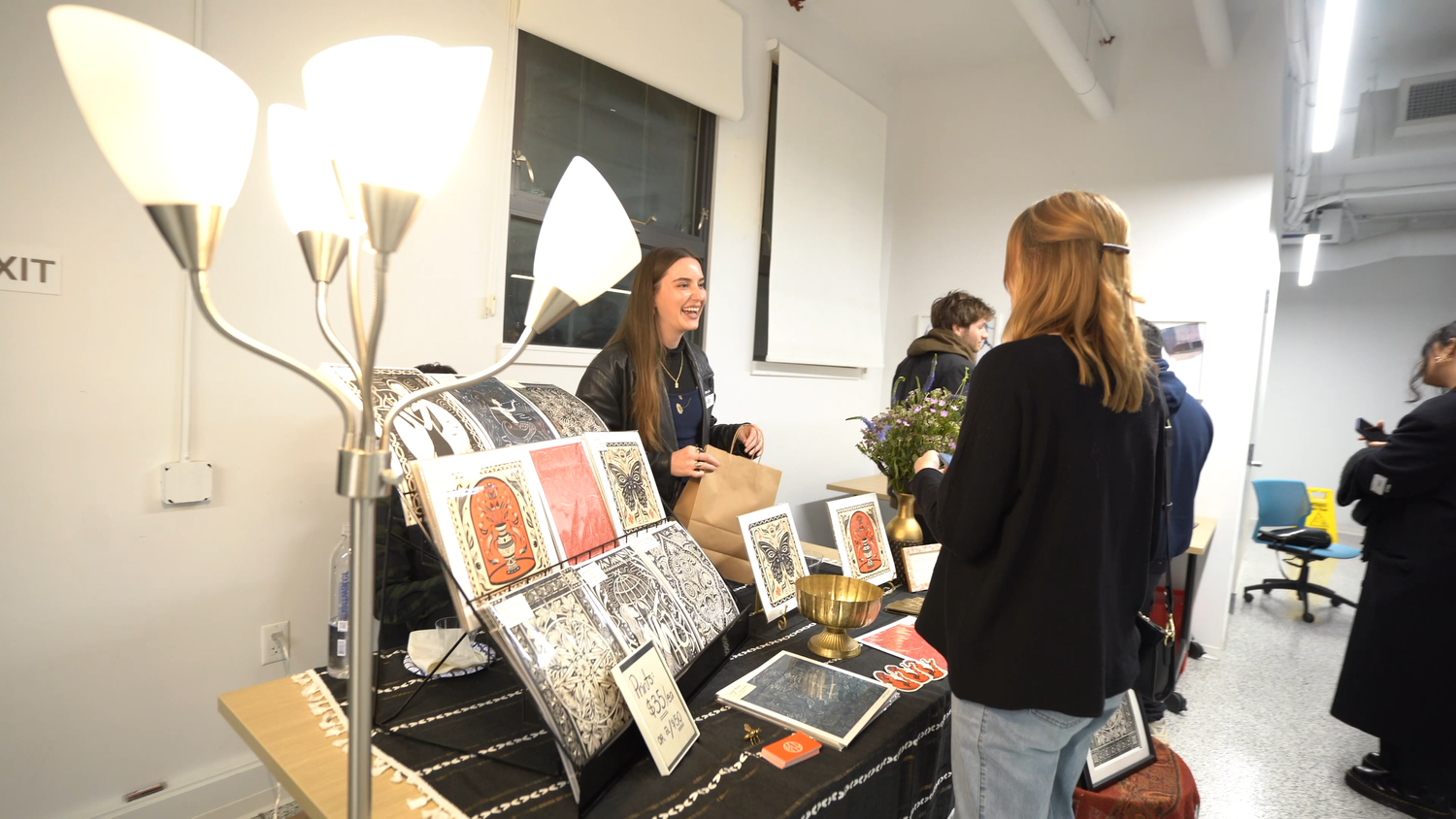 Visitors browse framed artwork on a display table.