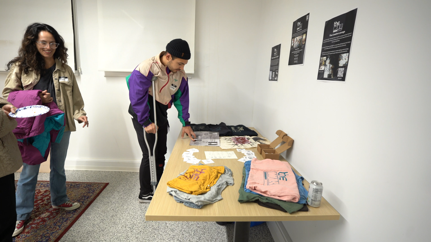 Guests examine clothing and printed goods on a table.