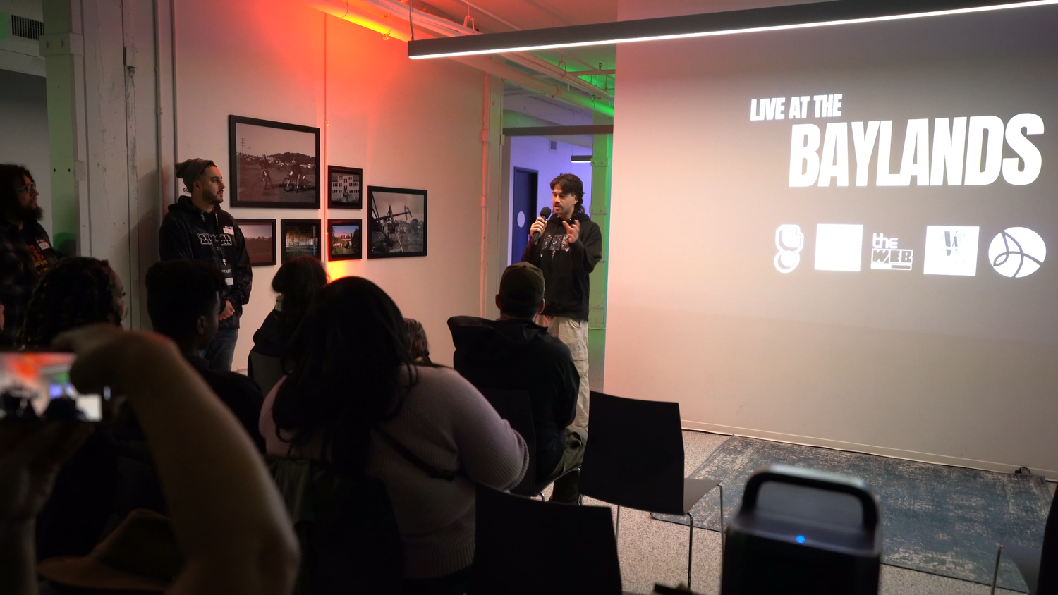 A presenter speaks beside the Live at the Baylands projection.