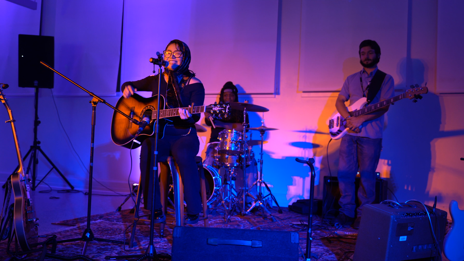 The band performs against a brightly colored wall.
