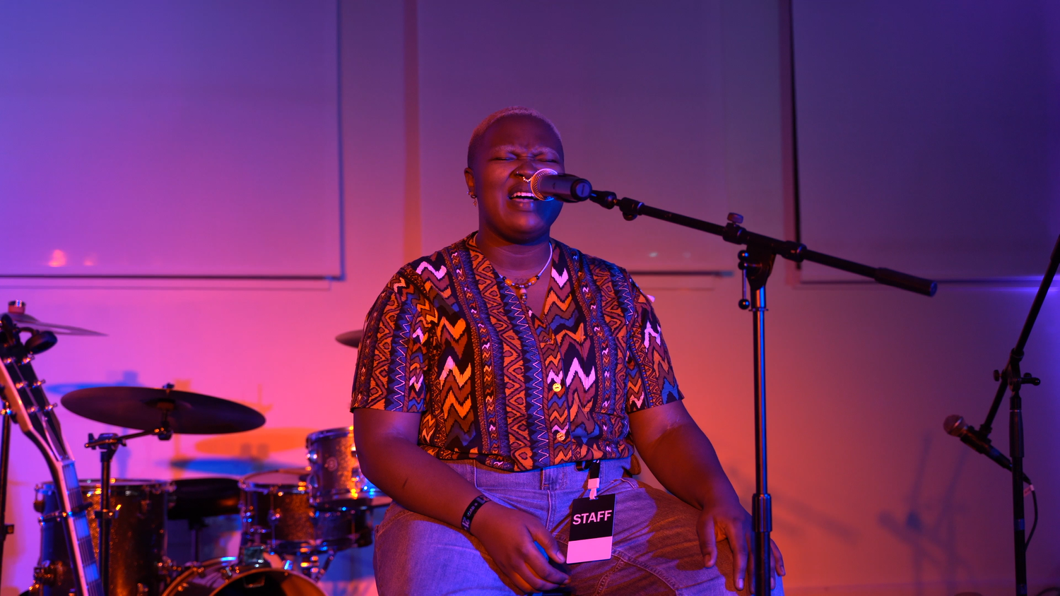 A vocalist speaks into a microphone beside an electric guitar.