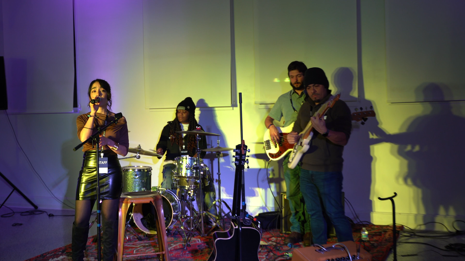 A vocalist performs in front of a drummer and two guitarists.