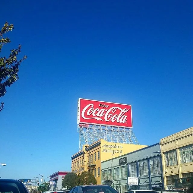 A Coca-Cola billboard above neighborhood buildings in daylight.