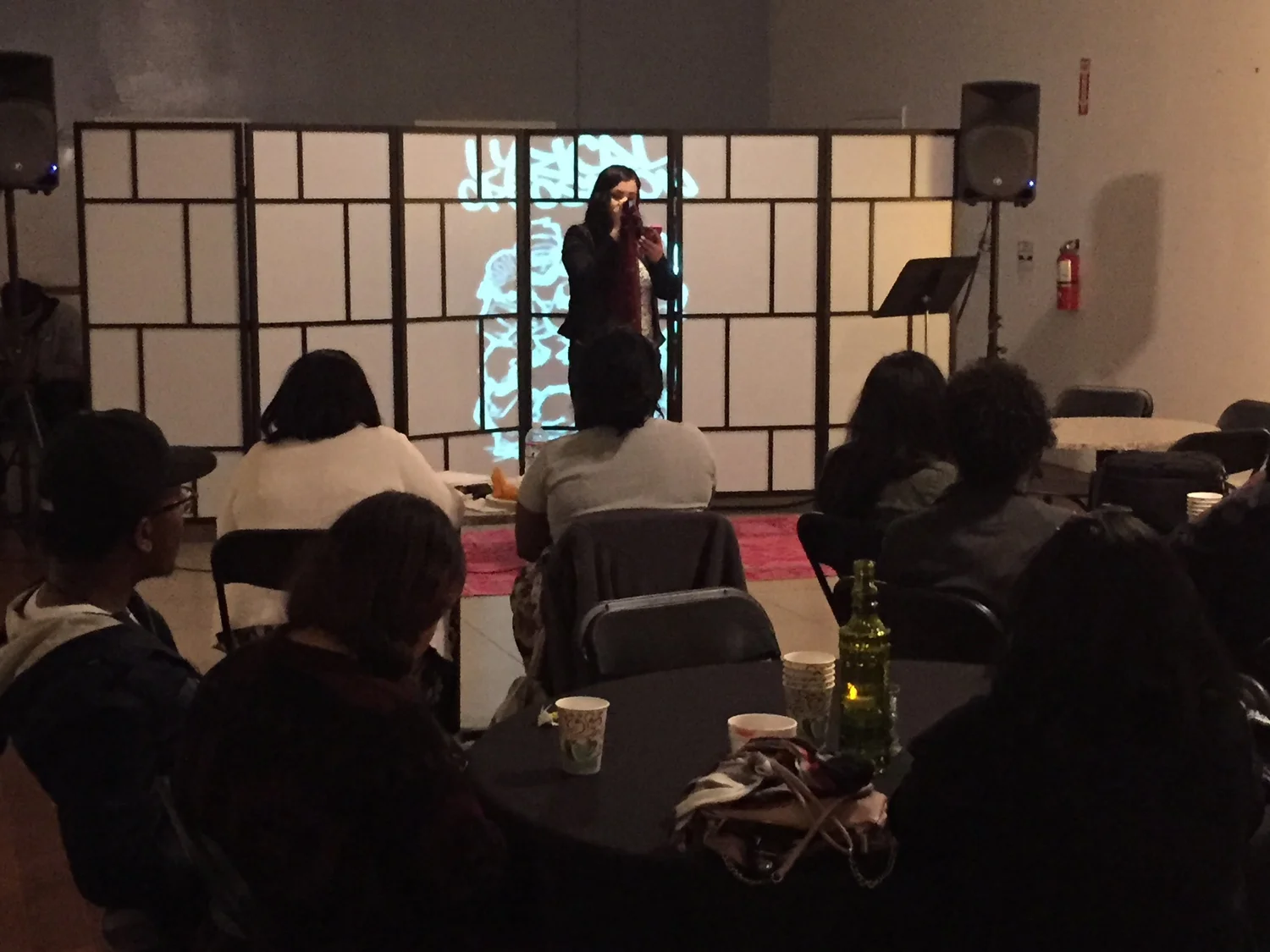 A performer speaks into a microphone before a seated audience.