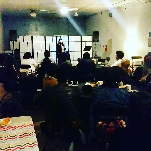 A seated audience watches the open-mic stage.