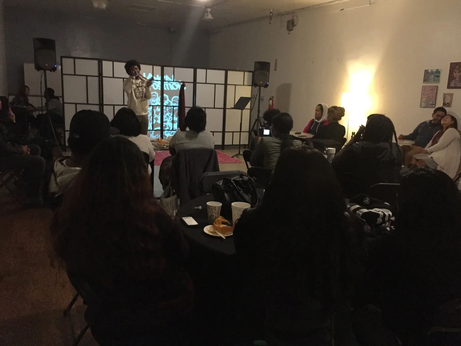 A performer onstage faces the seated open-mic audience.