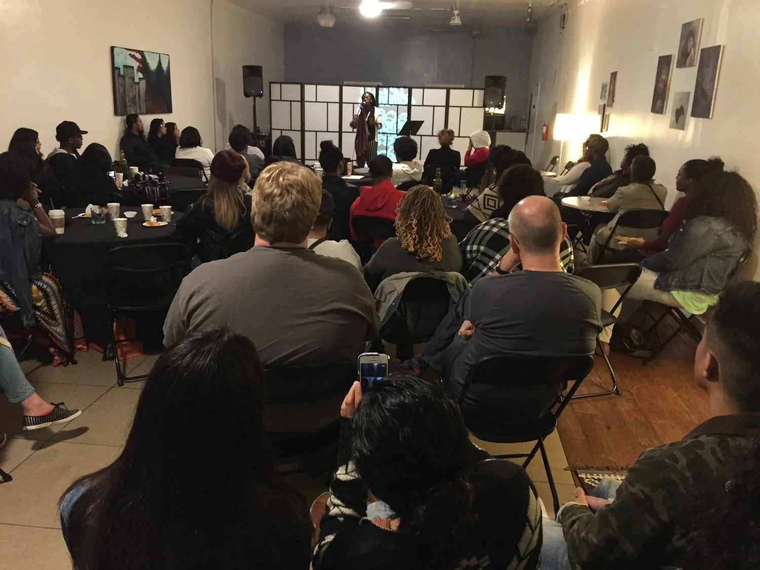 Audience members seated around tables at the open mic.
