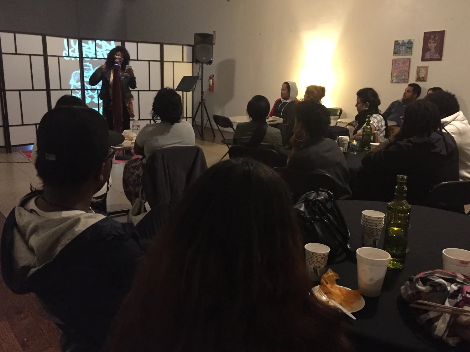 A performer onstage faces the seated open-mic audience.