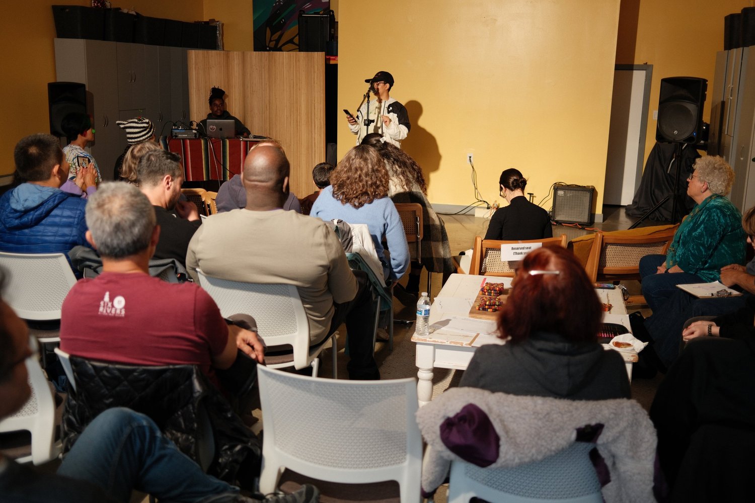 Audience watching a performer against the yellow wall.