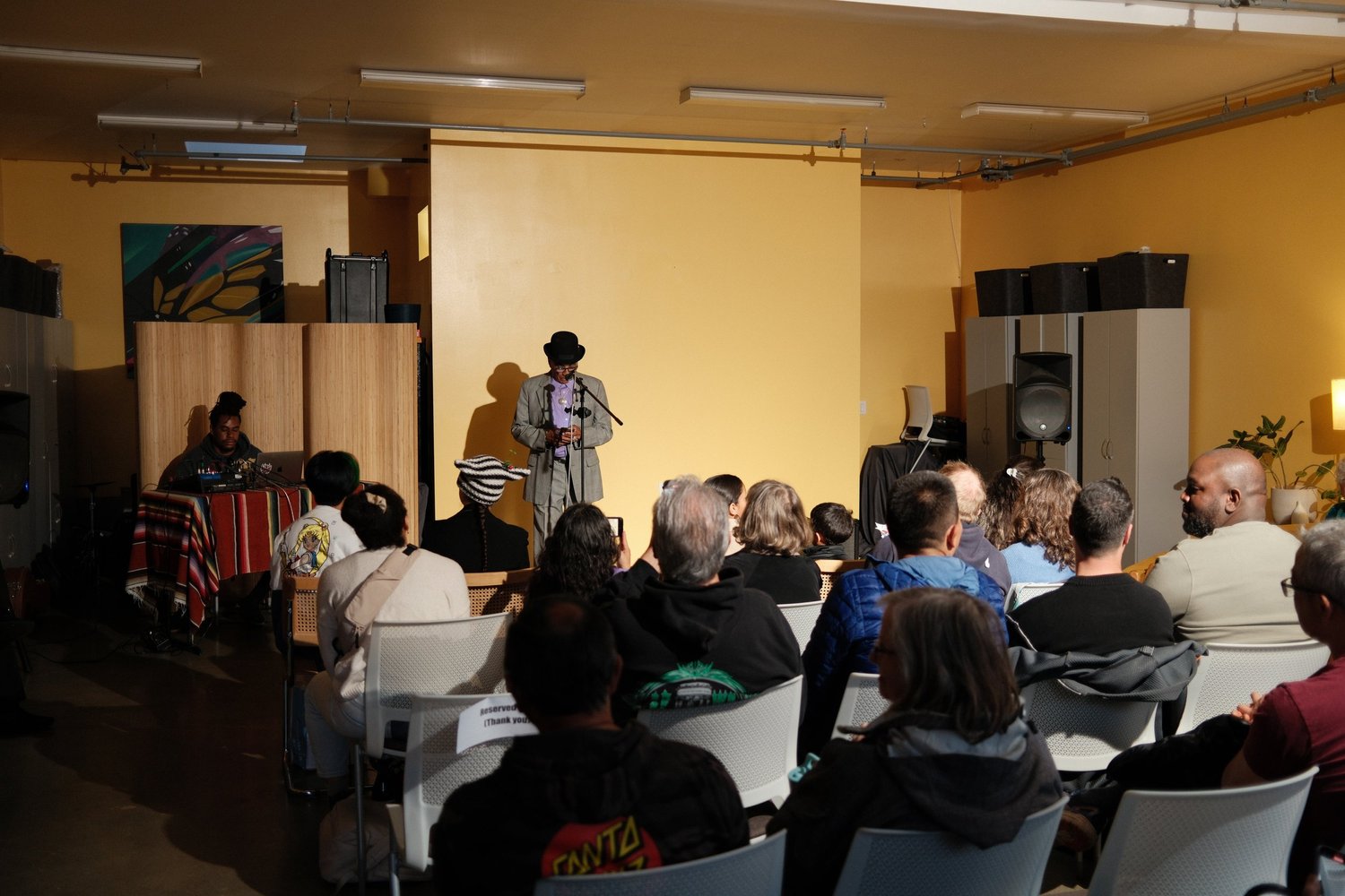 Performer wearing a brimmed hat reading at the microphone.