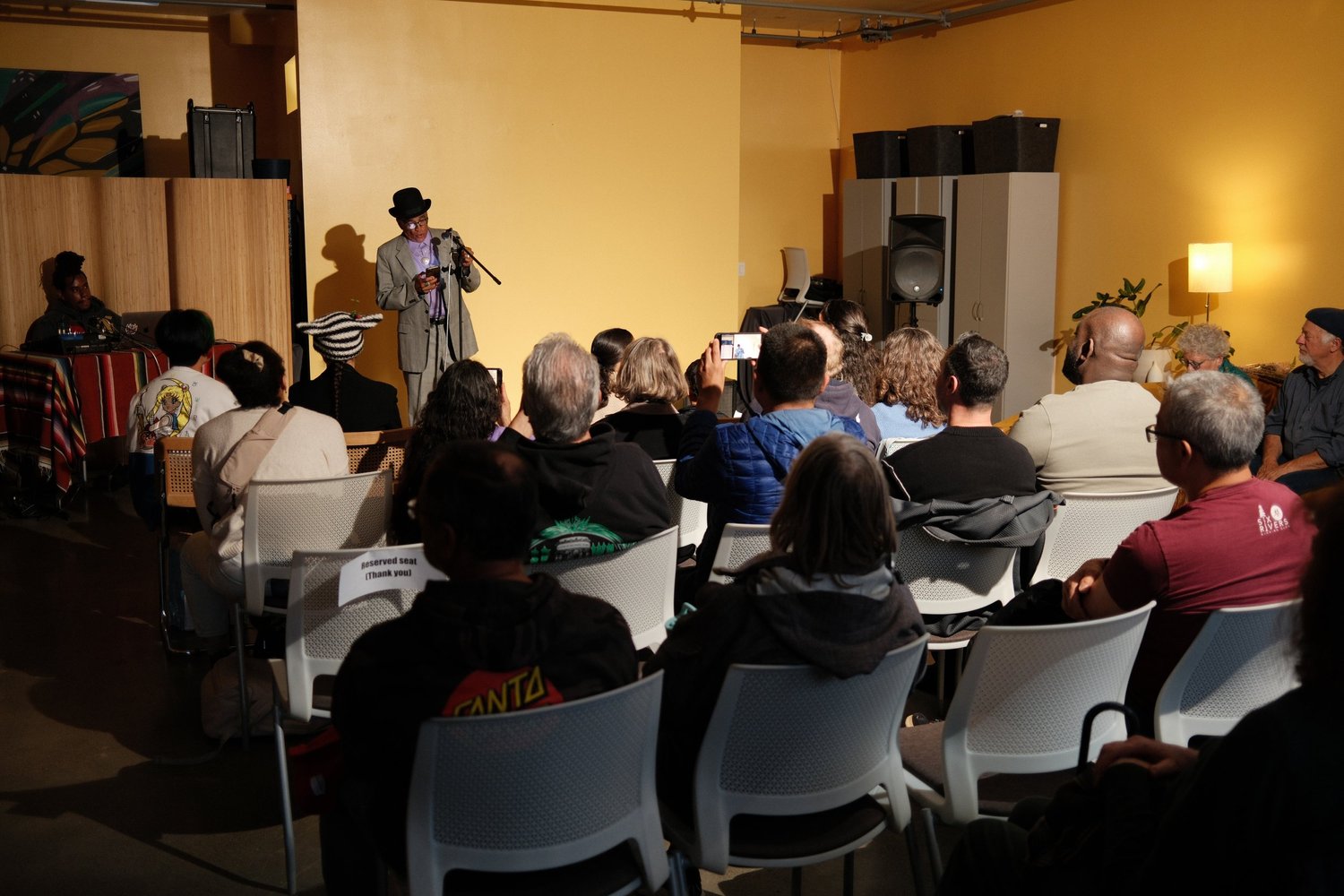 Performer reading from a printed page at the front of the room.