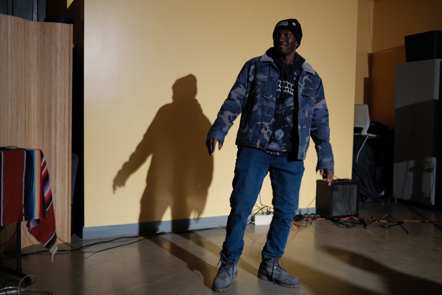 Performer standing beside a microphone with a shadow on the wall.
