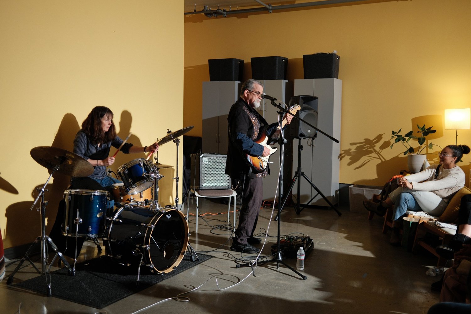 Guitarist performing into a microphone beside the drum kit.