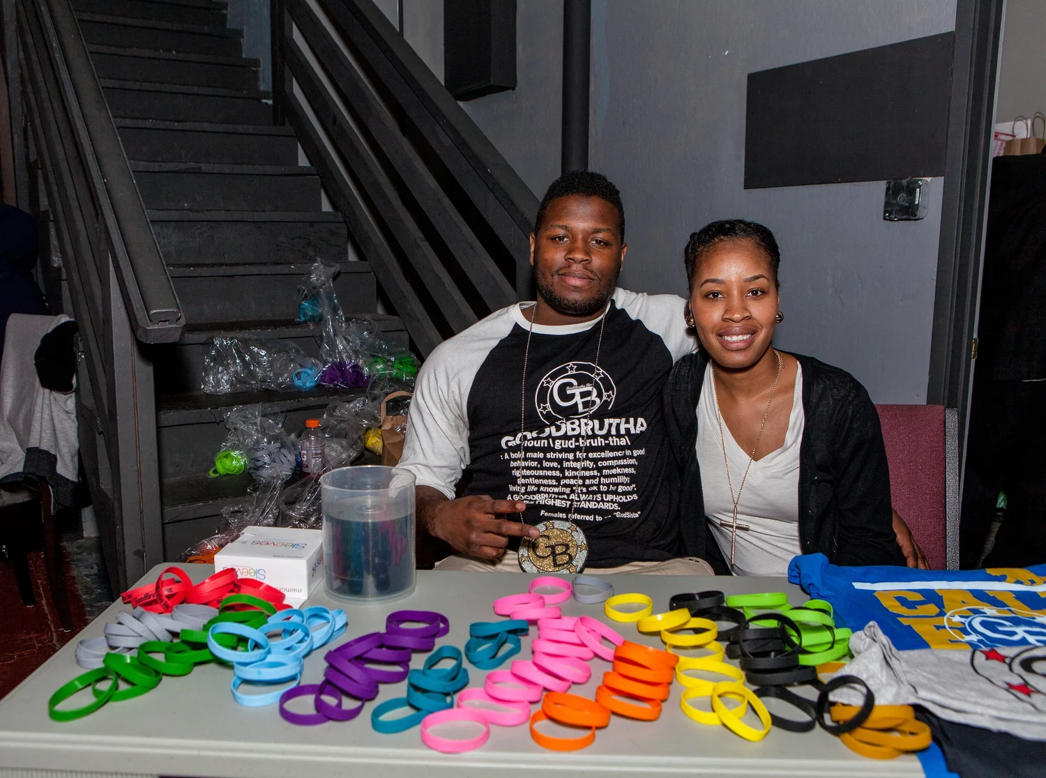 Two people seated behind a table of colorful wristbands.