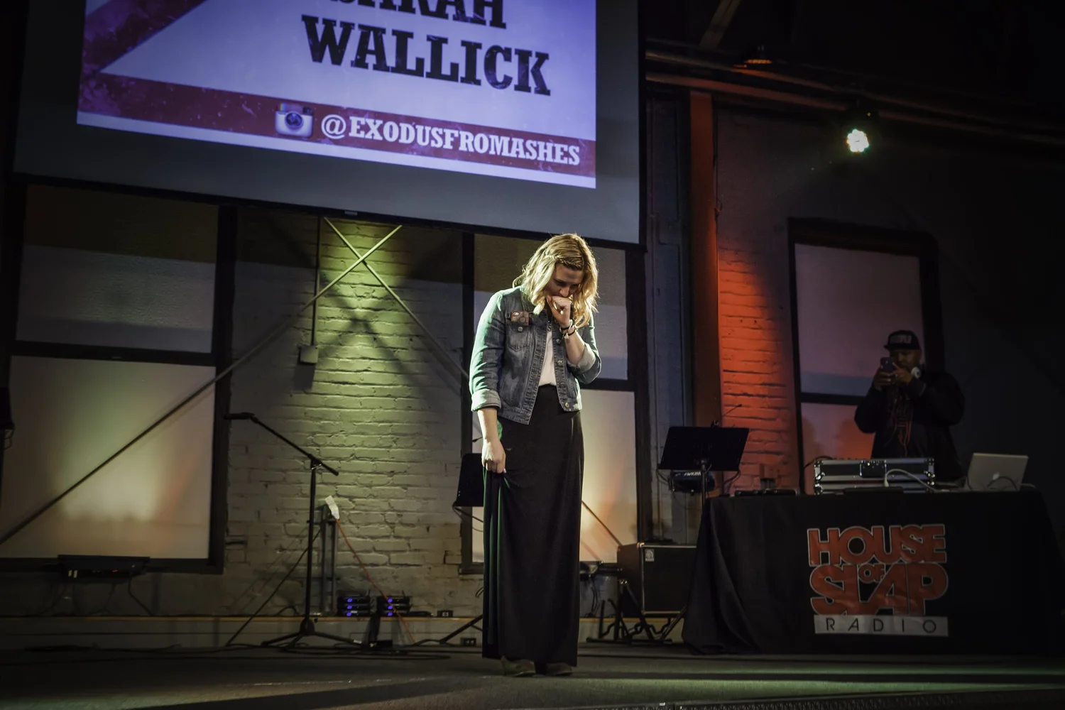 Vocalist leaning toward the microphone beneath a Sarah Wallick projection.