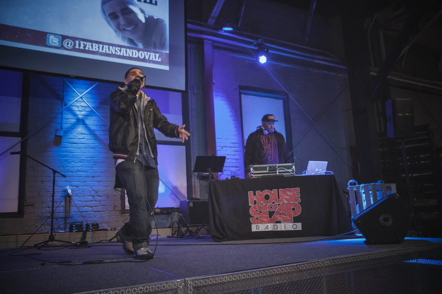 Performer addressing the audience beside a DJ table.