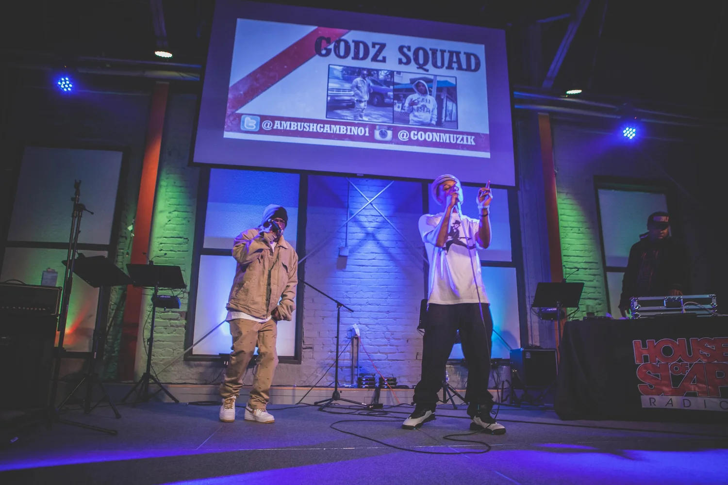 Two vocalists performing beneath a Godz Squad projection.