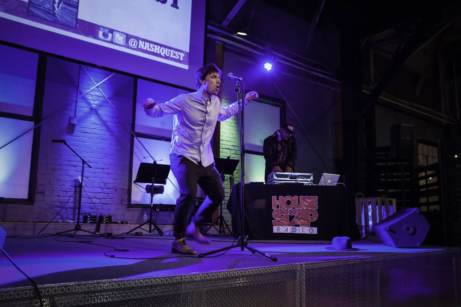 Performer gesturing onstage under blue and purple lights.