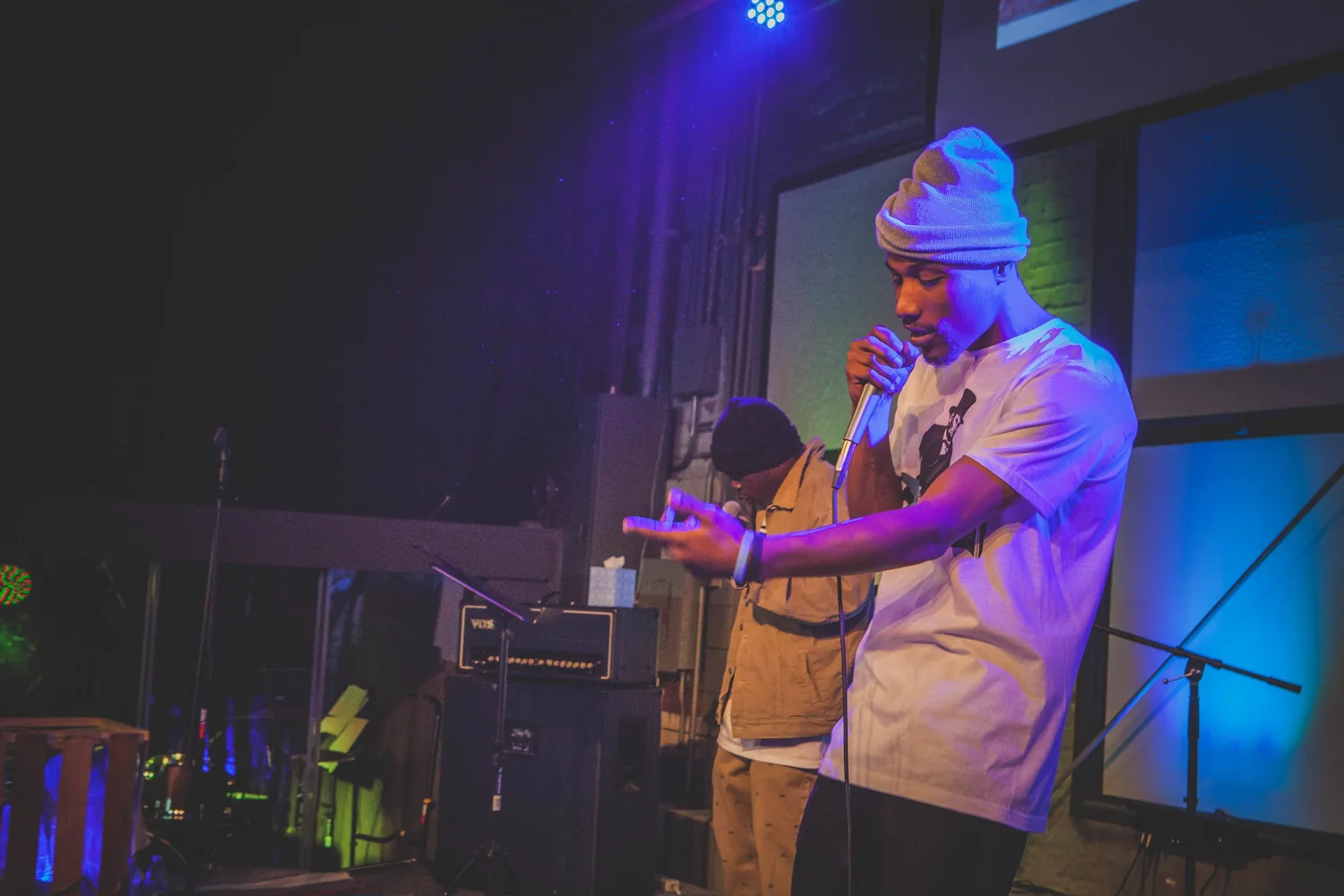Performer wearing a beanie gesturing with an open hand.