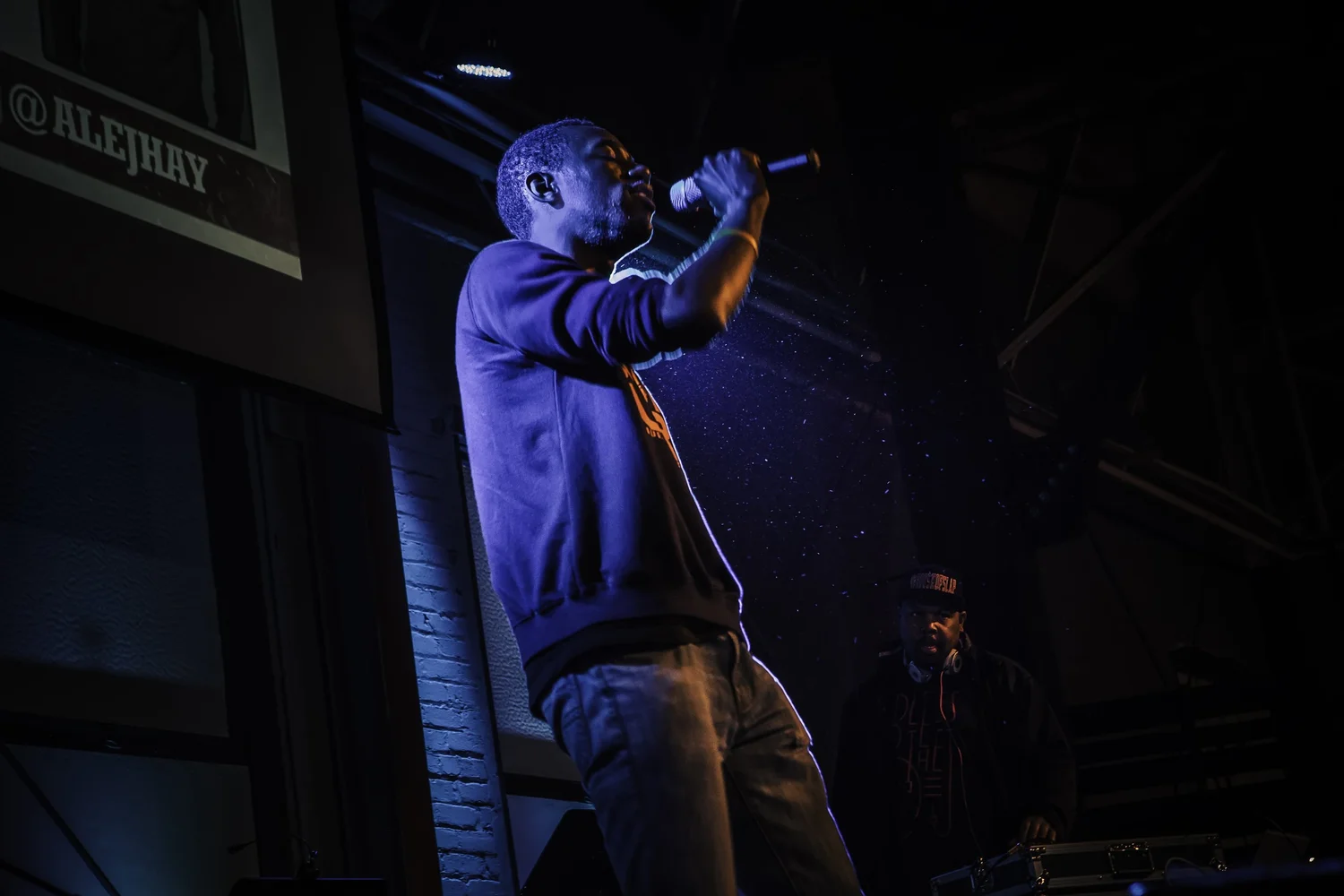 Vocalist performing in a dark hoodie under stage lights.