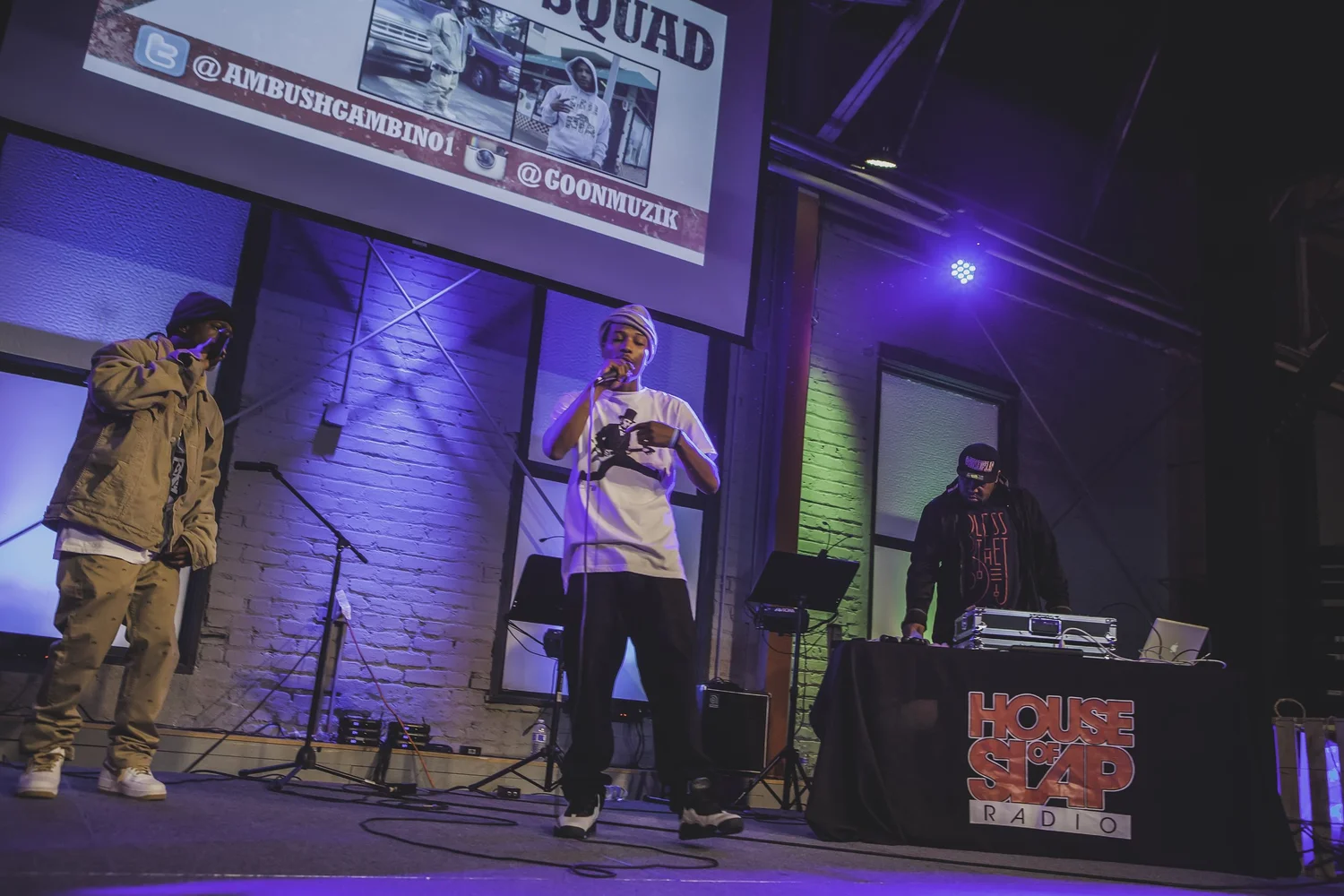 Two vocalists and a DJ under purple stage lighting.