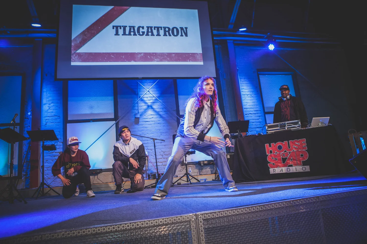 Dancer in a denim jacket performing beneath the Tiagatron projection.