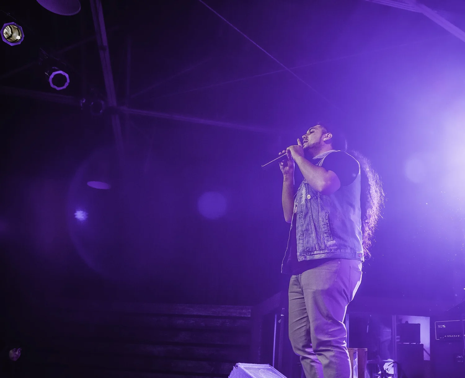 Vocalist with long hair performing in purple light.