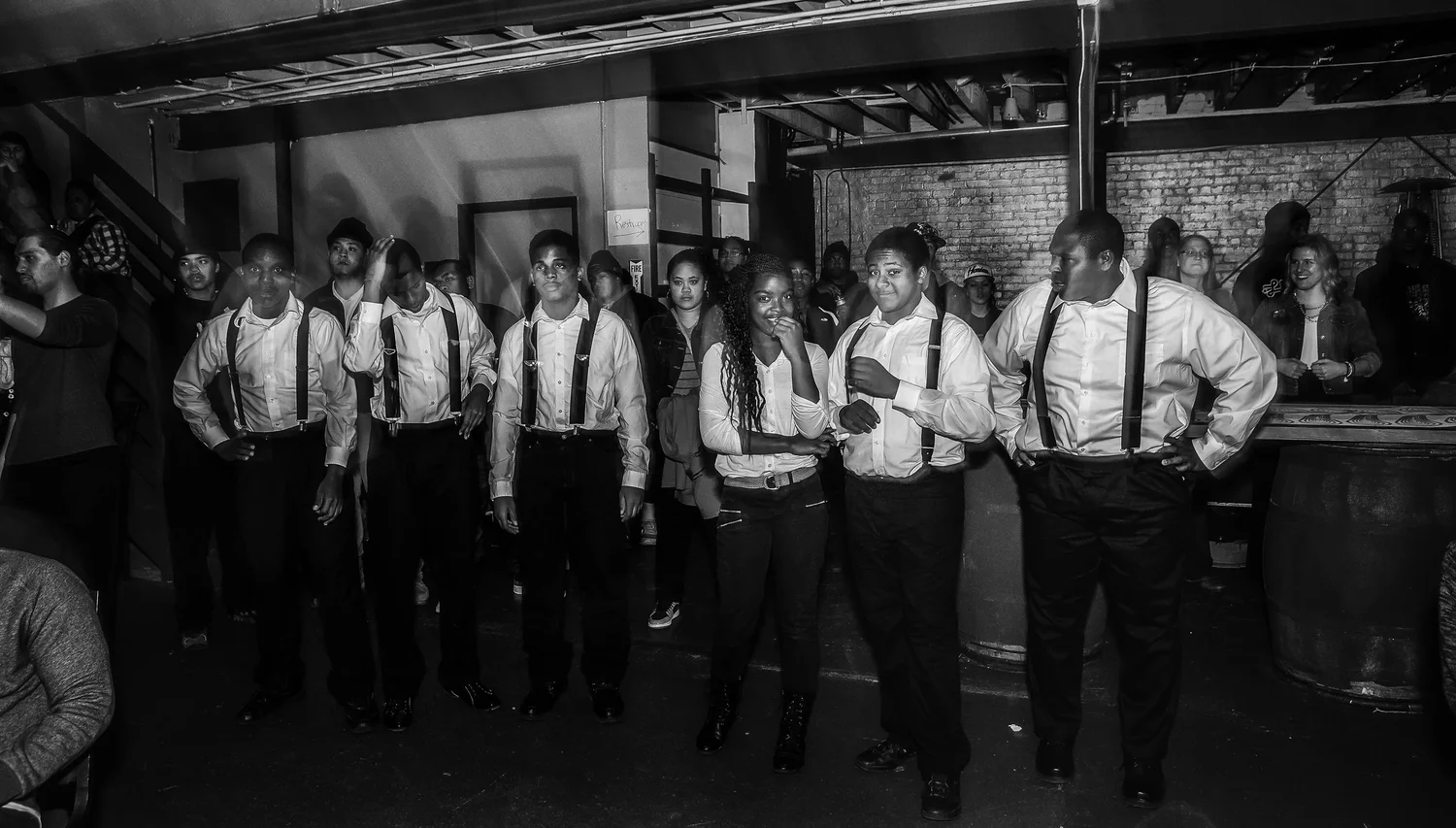 Black-and-white portrait of a dance group in matching shirts and suspenders.