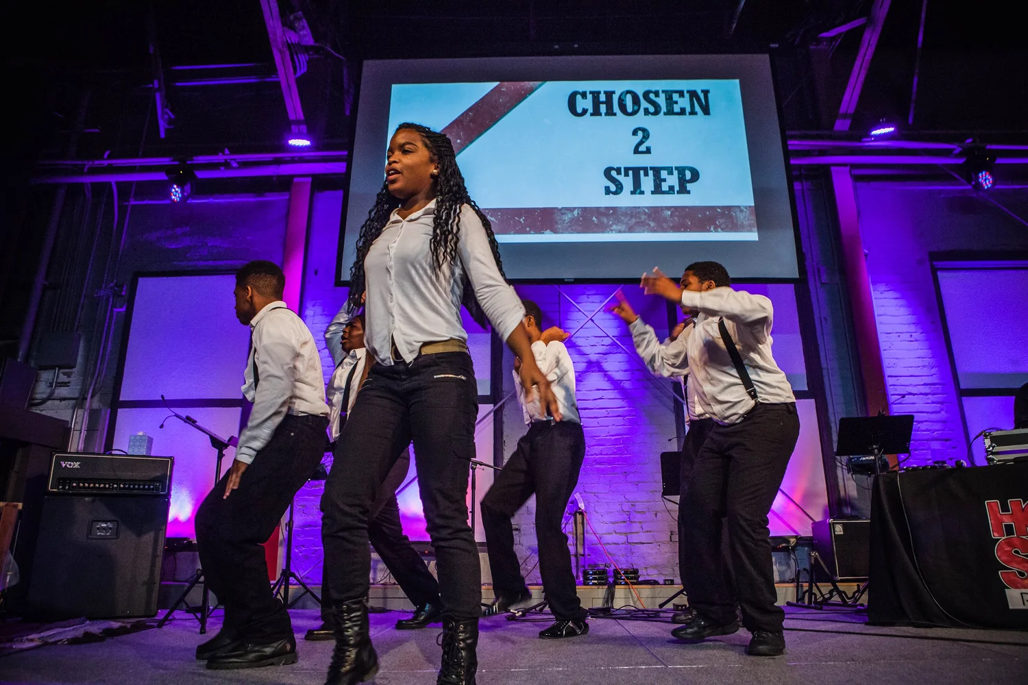 Dancers in matching shirts and suspenders moving in formation.