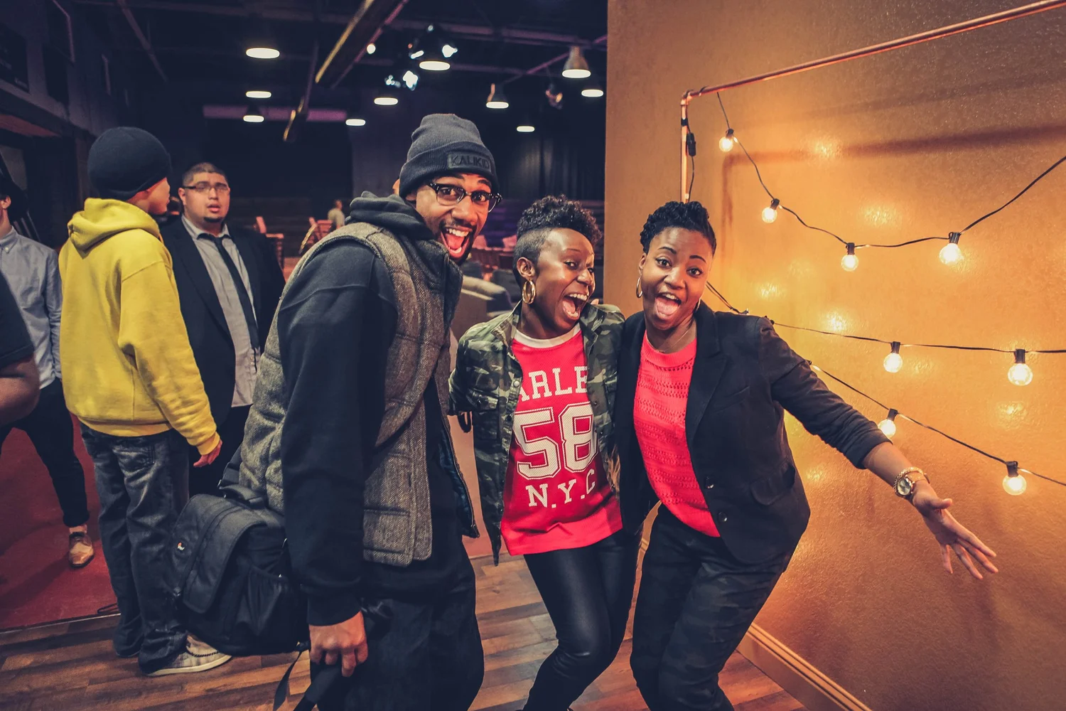 Three smiling attendees posing beside a wall with string lights.