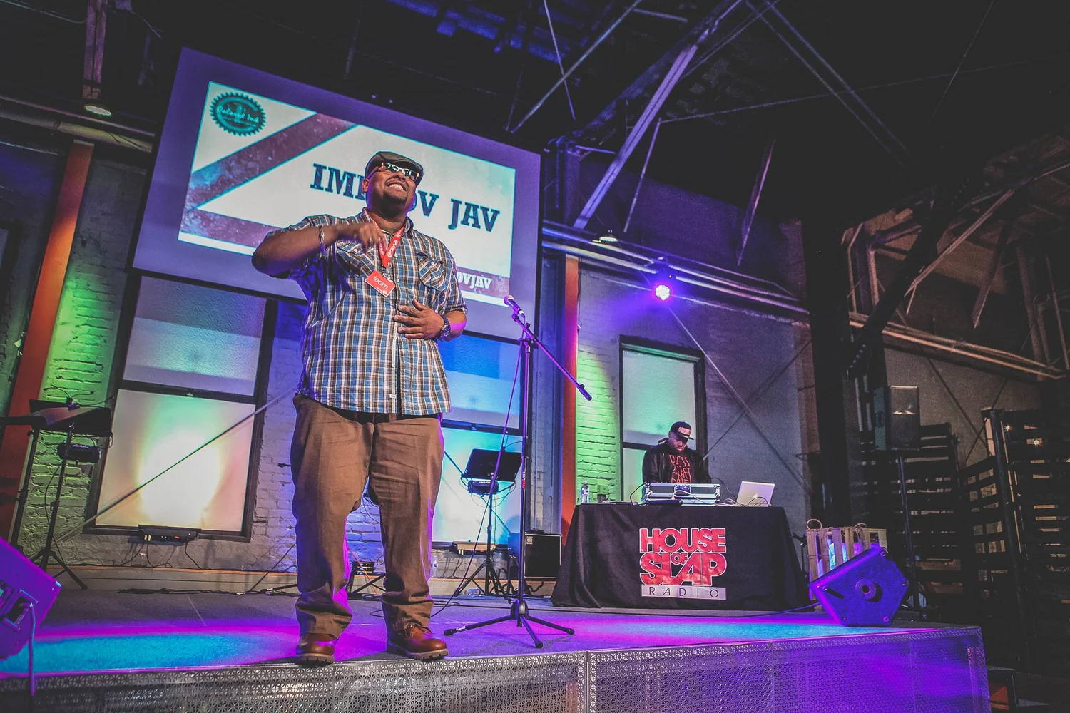 Performer in a checked shirt gesturing at the microphone.