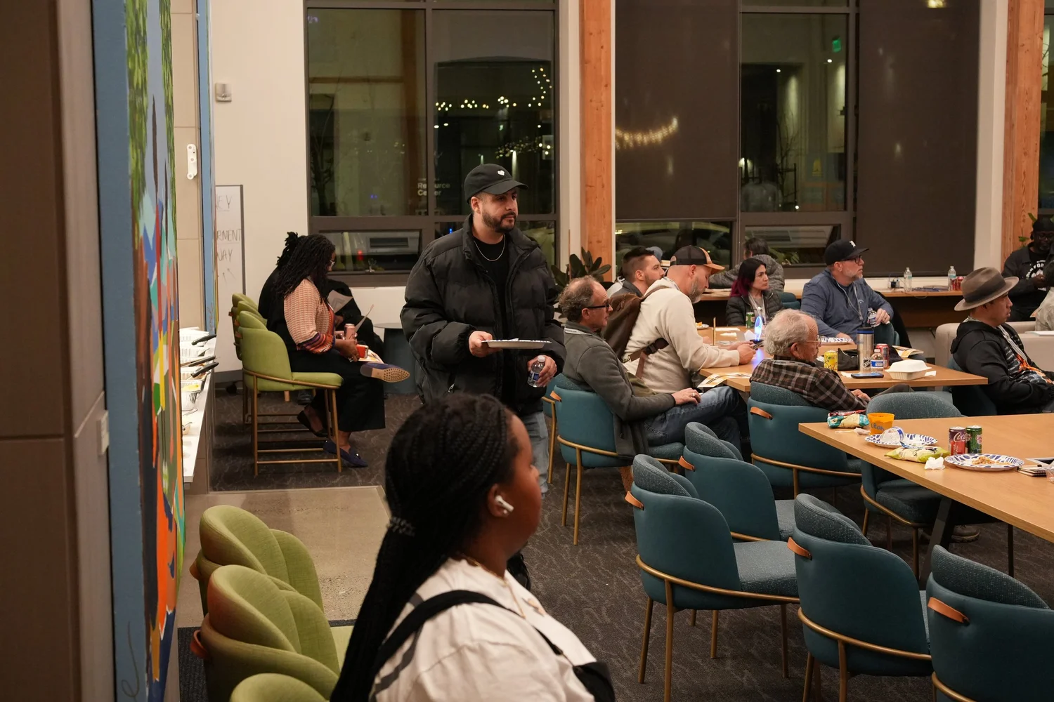 Guests seated around tables and sofas listen to the community program.