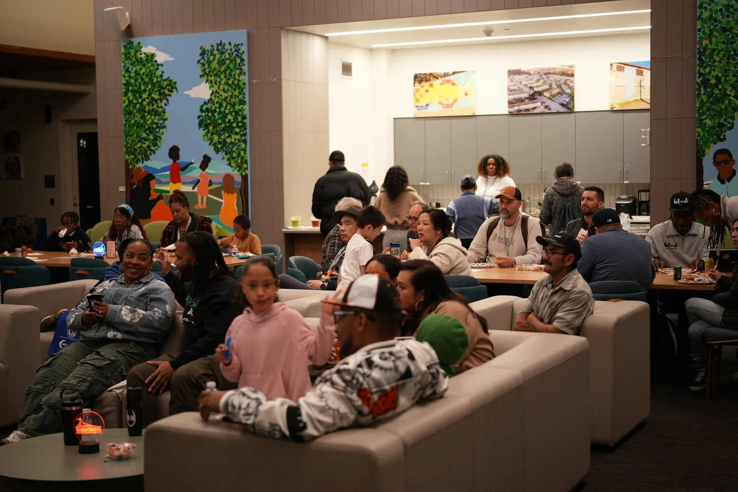 Guests seated around tables and sofas listen to the community program.