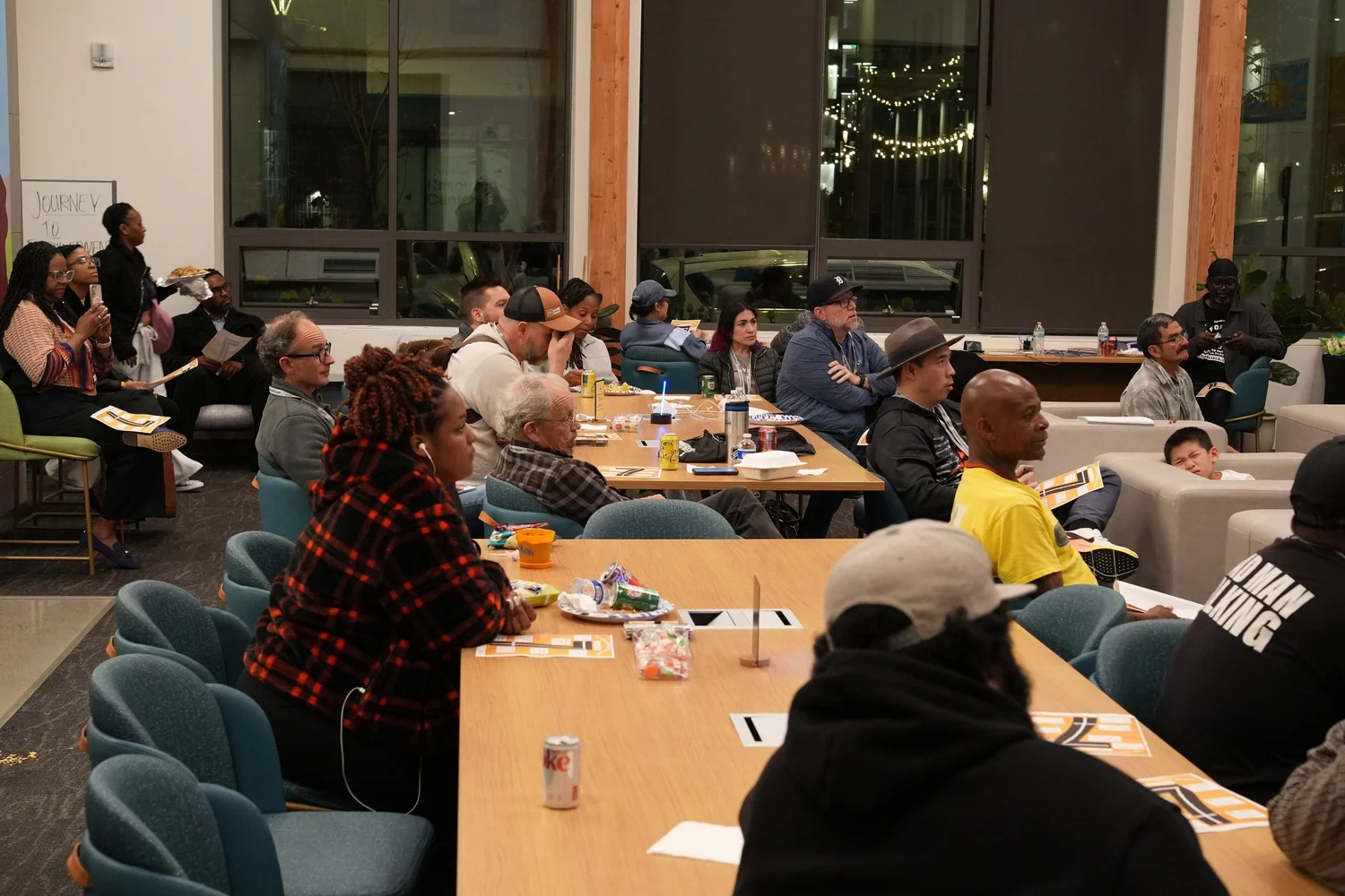 Guests seated around tables and sofas listen to the community program.