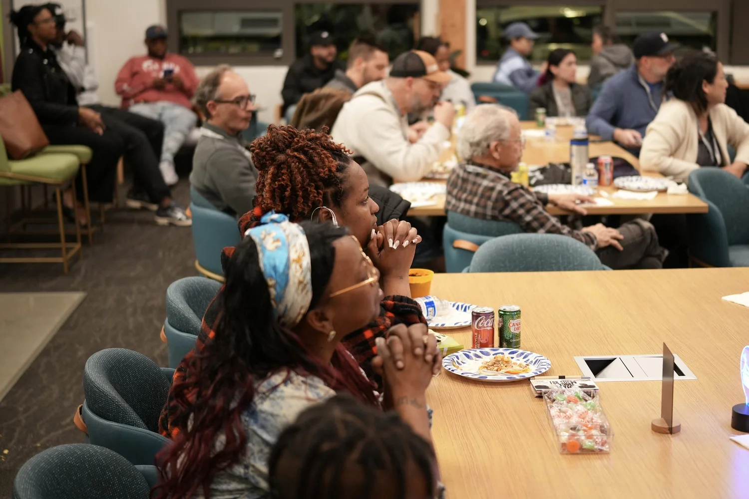 Guests seated around tables and sofas listen to the community program.