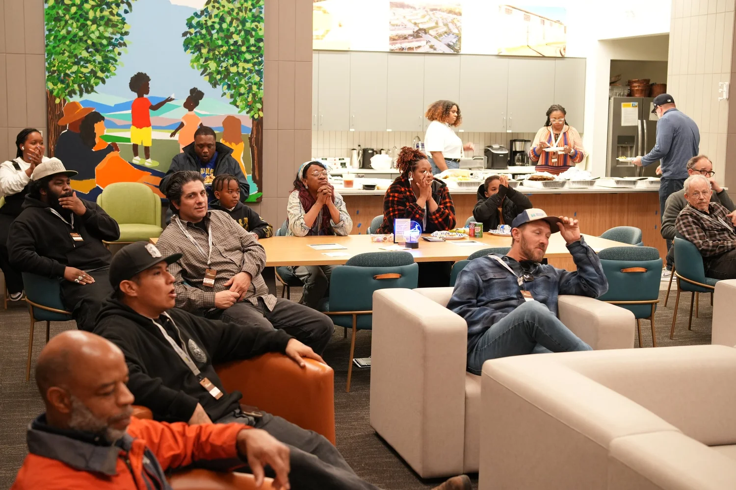 Guests seated around tables and sofas listen to the community program.