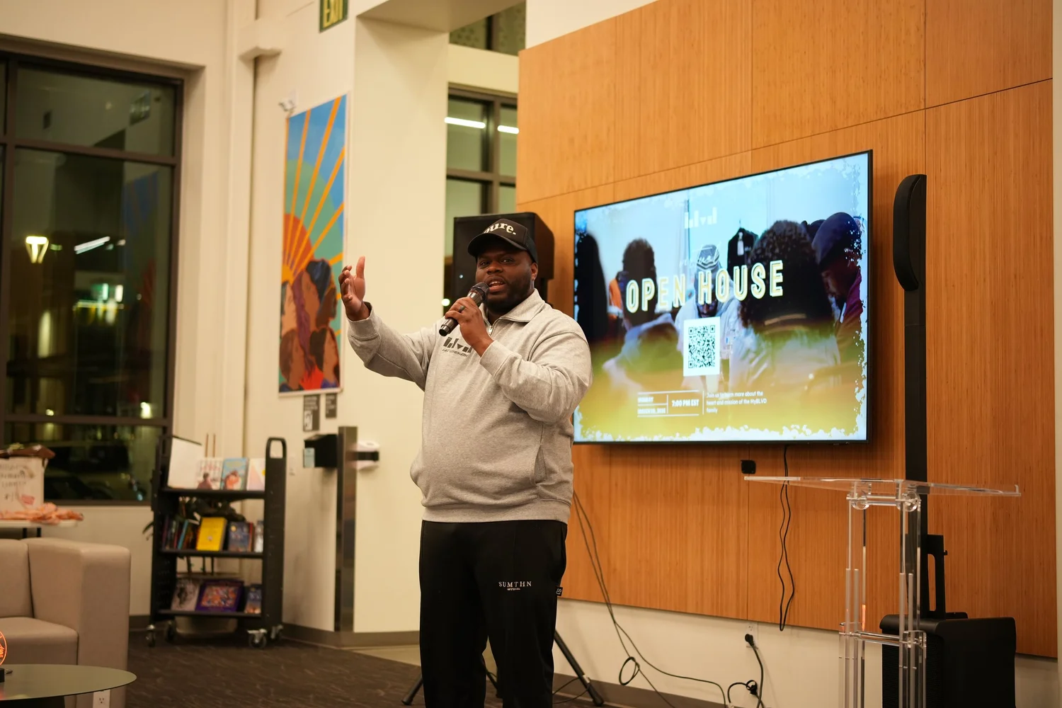 Speaker raising a hand beside the open-house display.