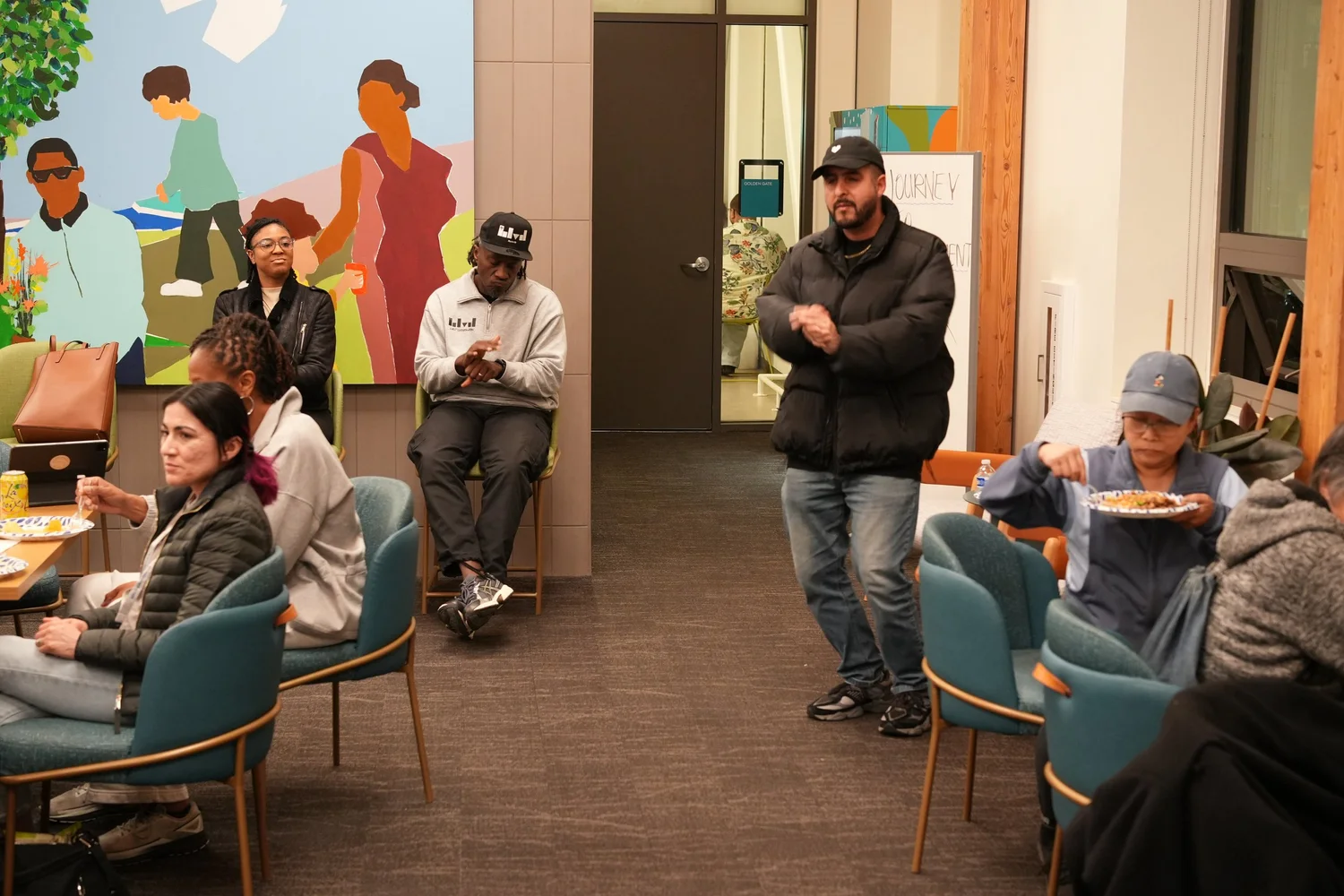 Attendees standing and sitting beneath a colorful wall mural.