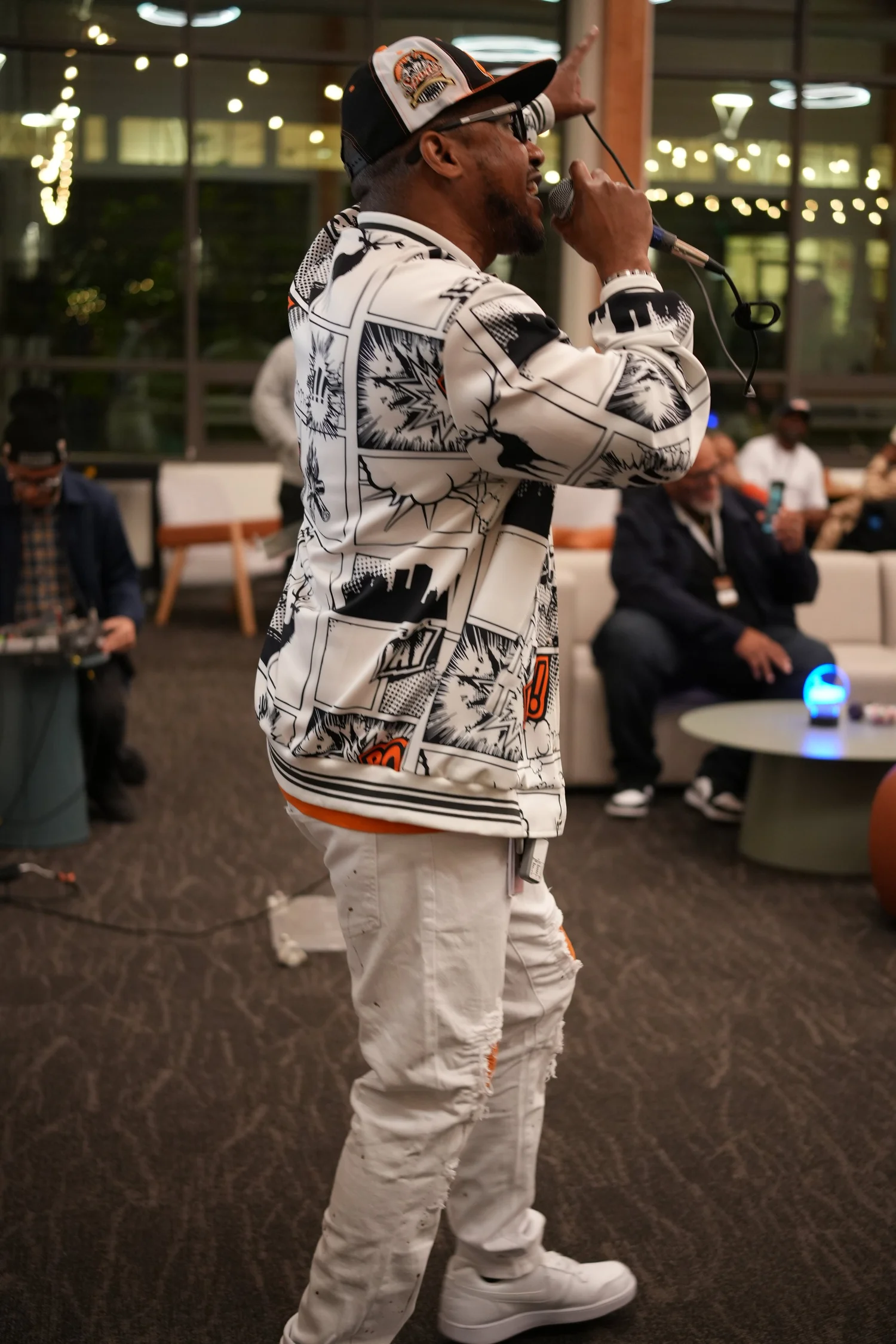 Performer in a patterned jacket holding a microphone in the community lounge.