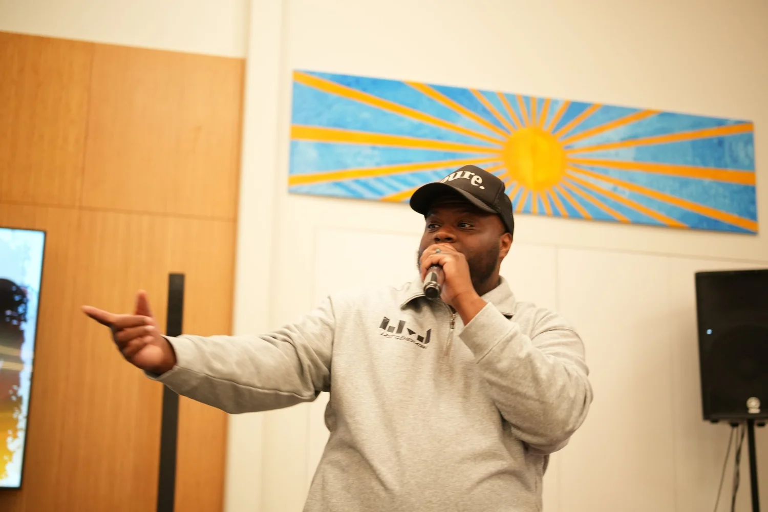 Close view of a performer in a light sweatshirt gesturing with a microphone.